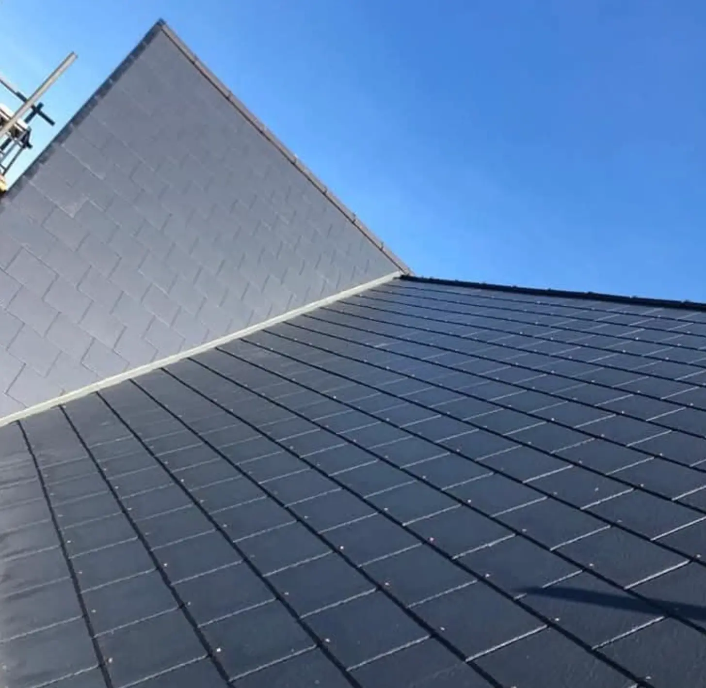 Completed dark slate roof with finished ridge and clean verge detail against a blue sky