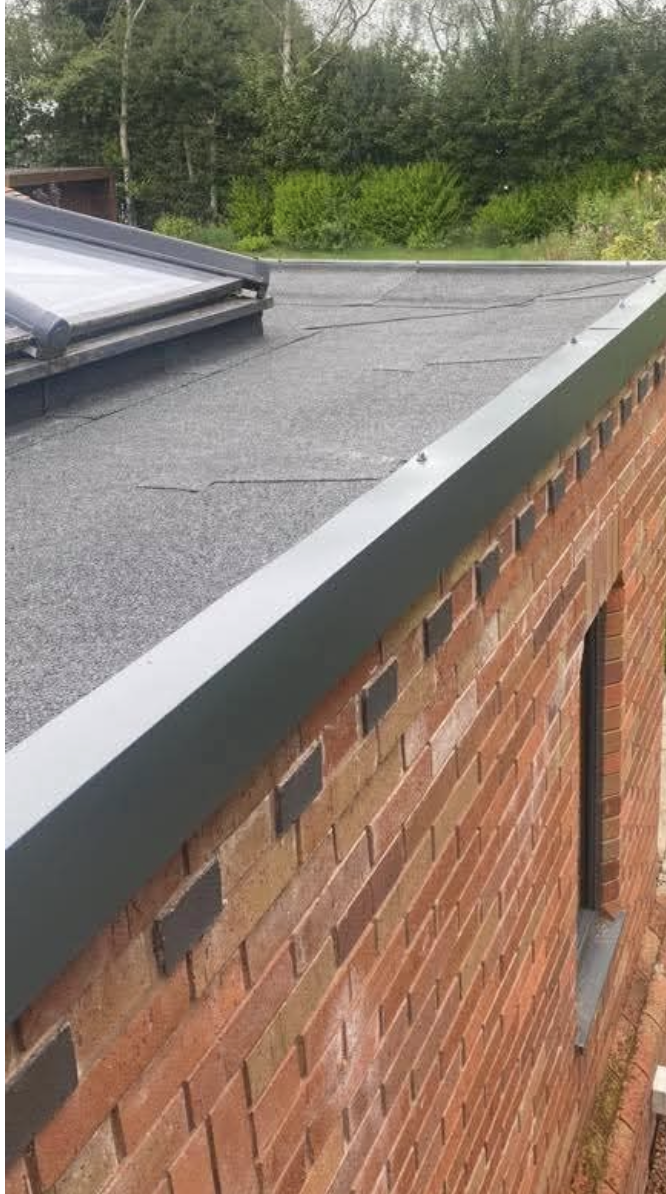 Grey metal drip trim fitted along the edge of a felt flat roof above red brickwork