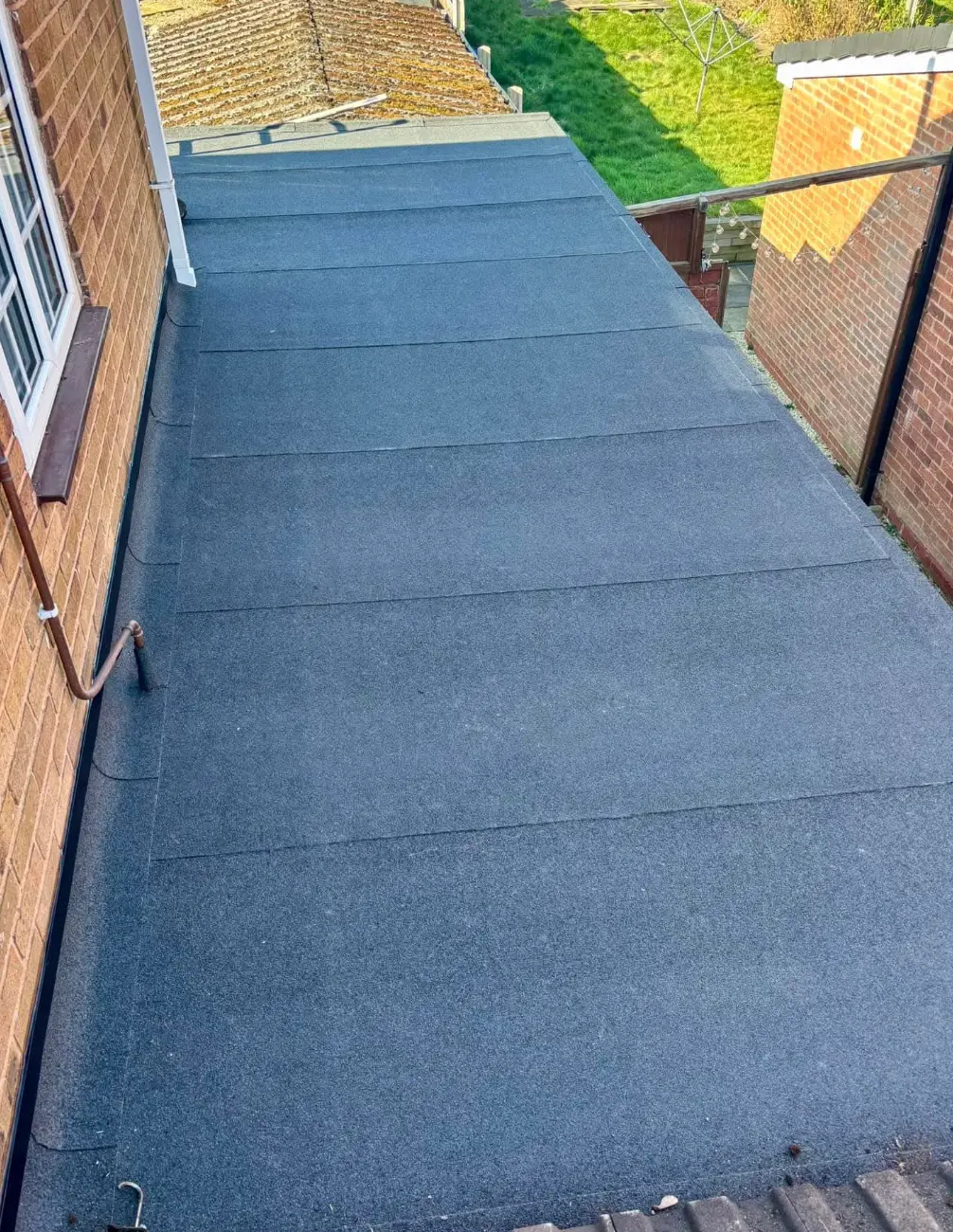 Newly laid grey felt flat roof running alongside a brick wall to a gutter