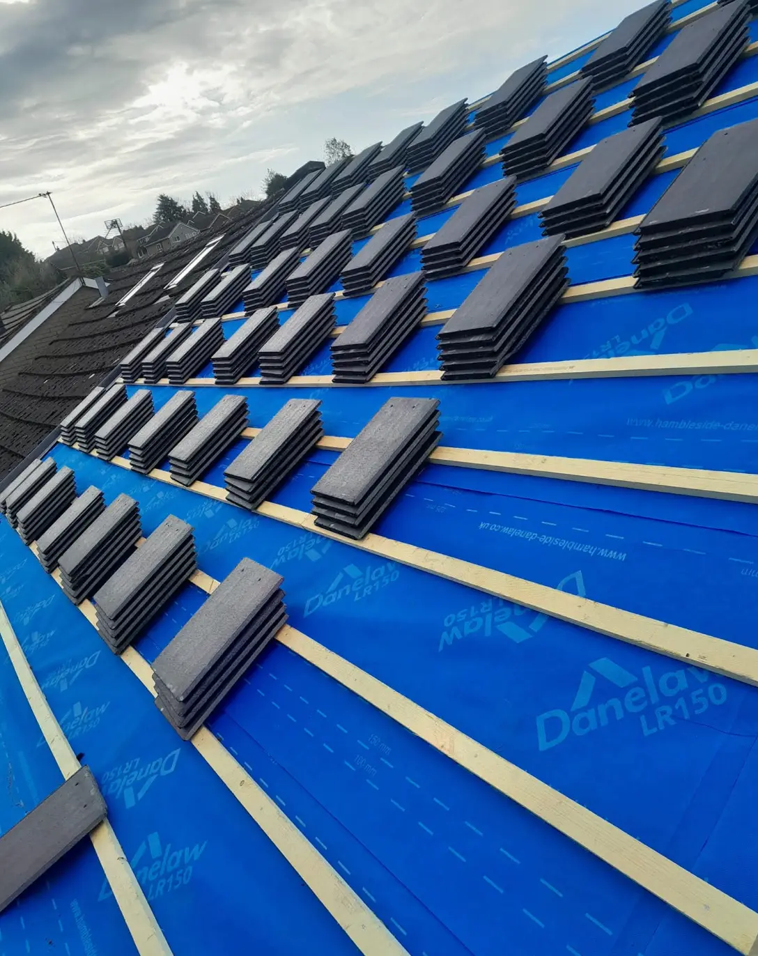 Roof stripped to new blue breathable membrane and battens with slates stacked ready to lay