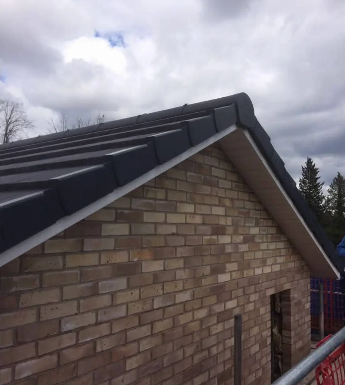 New build house with dark tiled roof and neatly finished gable verge over yellow brickwork