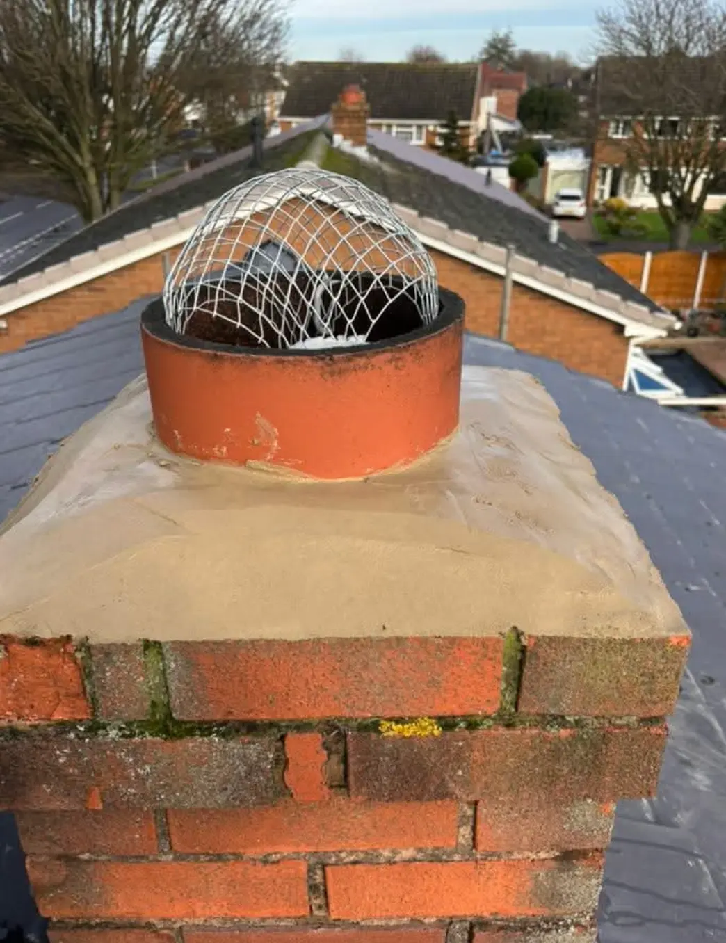 Chimney stack with new sand-coloured flaunching and a wire bird guard over the pot