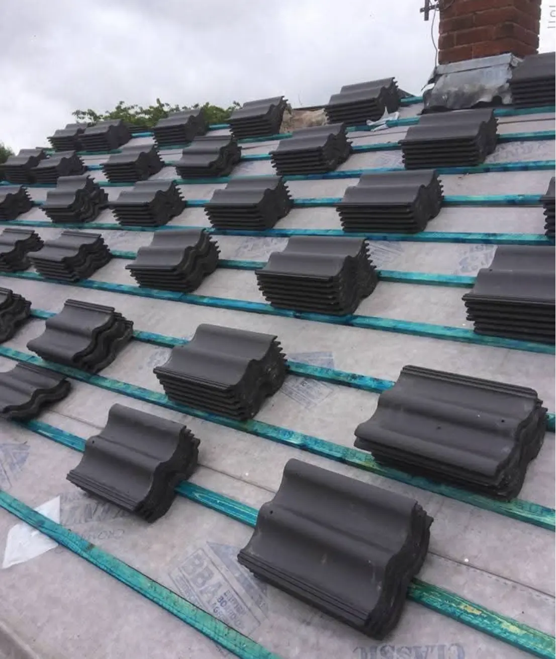 Stacks of grey interlocking roof tiles loaded out across new battens and membrane