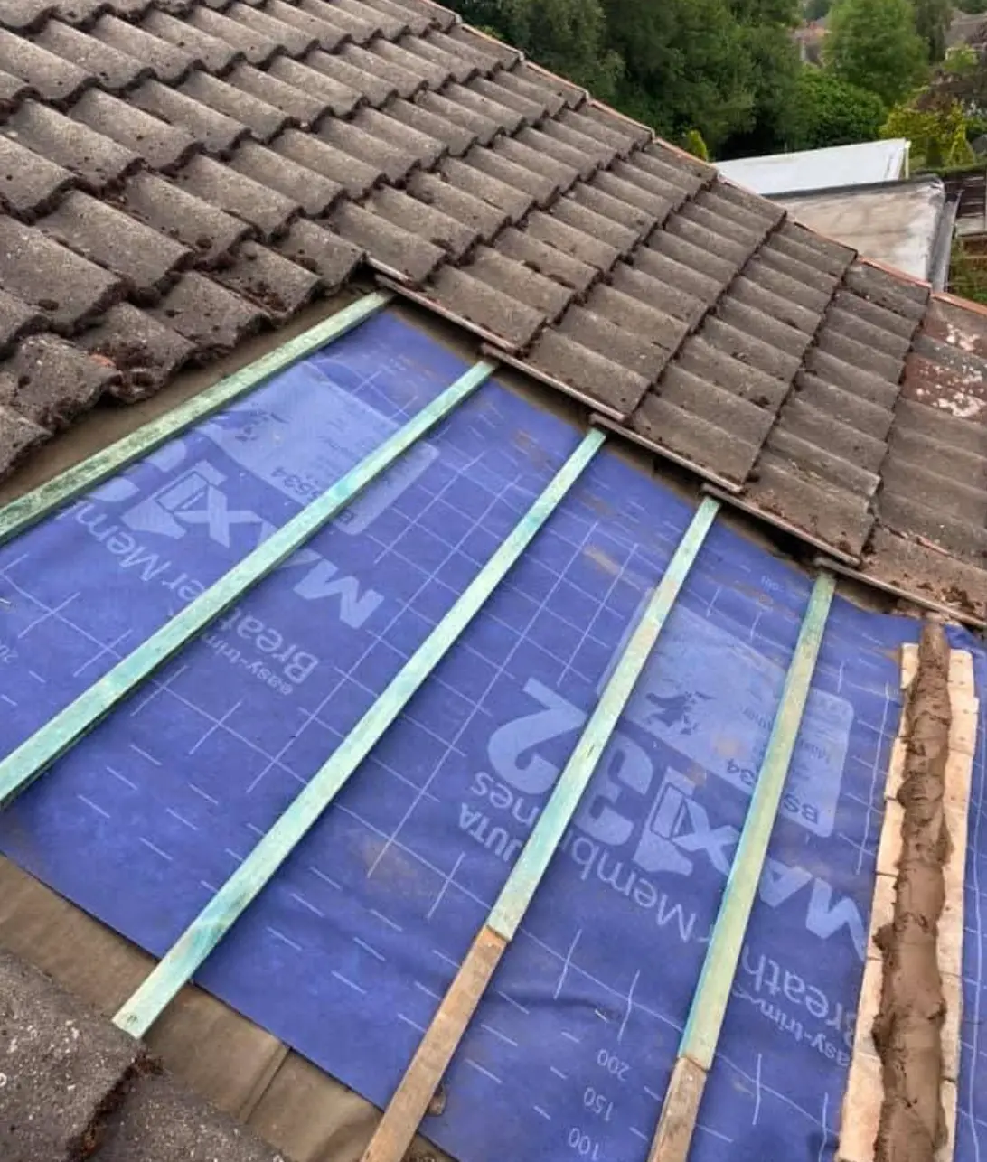Roof half stripped with new blue breathable membrane and battens laid beside old tiles