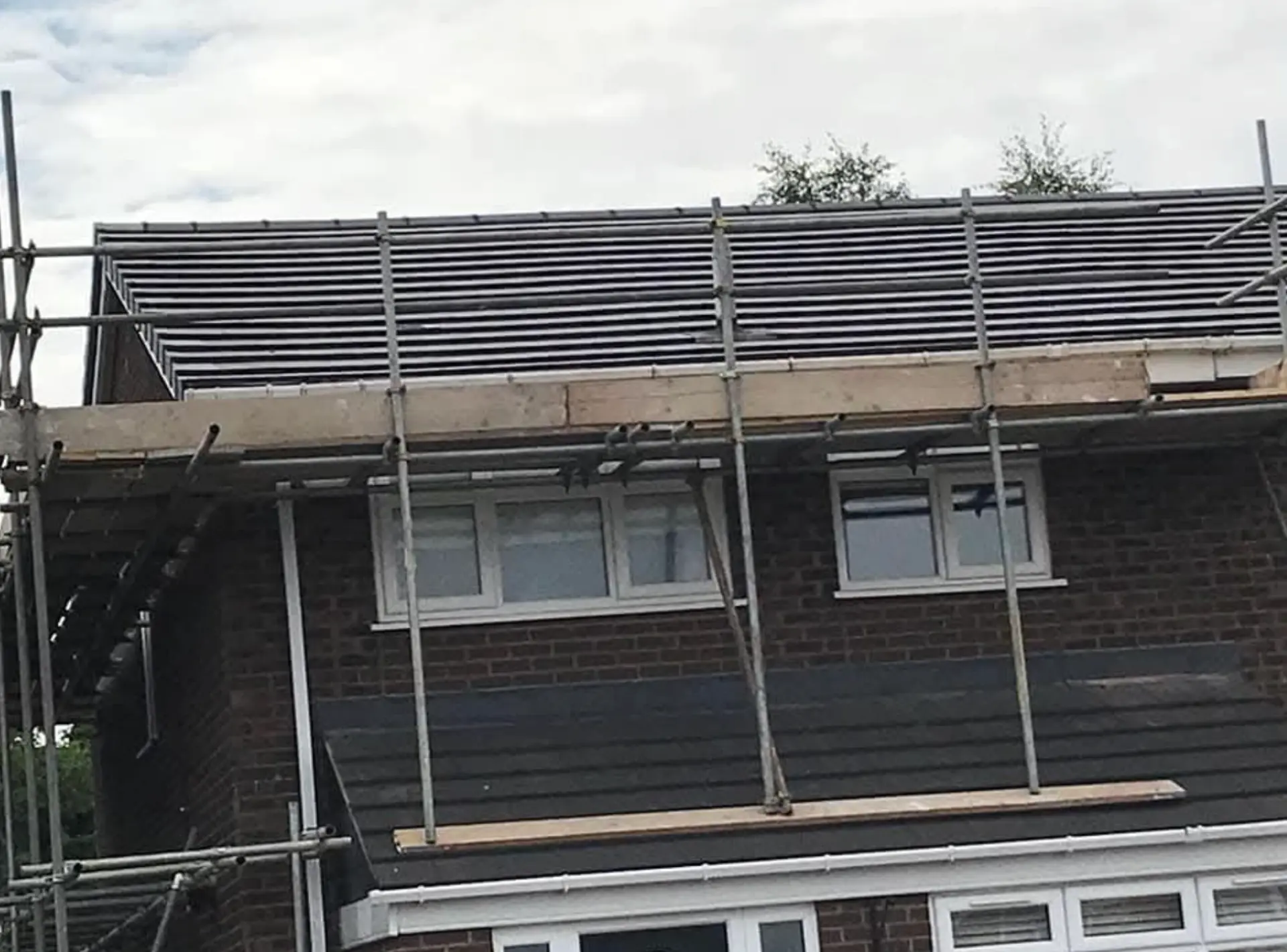 Semi-detached house roof being re-tiled with scaffolding erected around the eaves